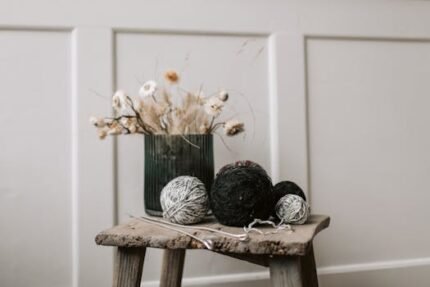 A rustic still life featuring yarn and dried flowers on an old stool.